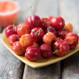 Talerz pełen soczystych, czerwonych i pomarańczowych owoców, przypominających egzotyczną wiśnię krzyżówkę.
